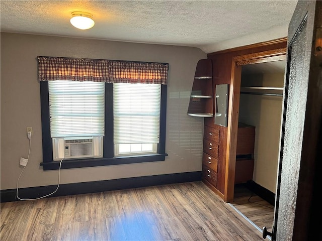unfurnished bedroom with a textured ceiling, wood finished floors, a closet, and cooling unit