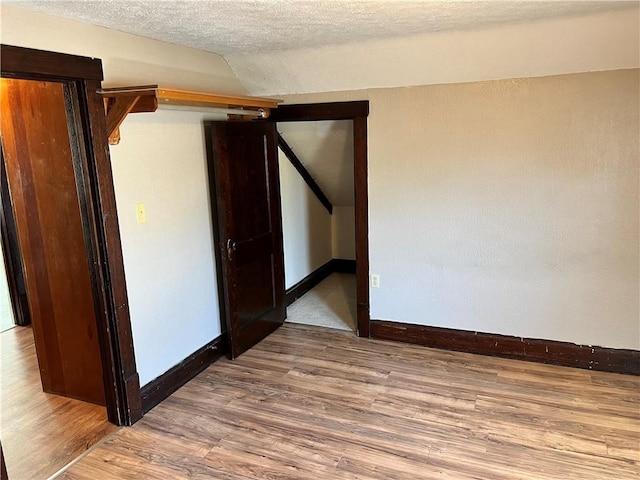 empty room featuring a textured ceiling, baseboards, vaulted ceiling, and wood finished floors