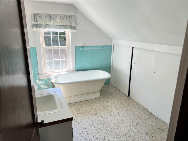 bathroom featuring lofted ceiling, a wainscoted wall, tile walls, a soaking tub, and tile patterned floors