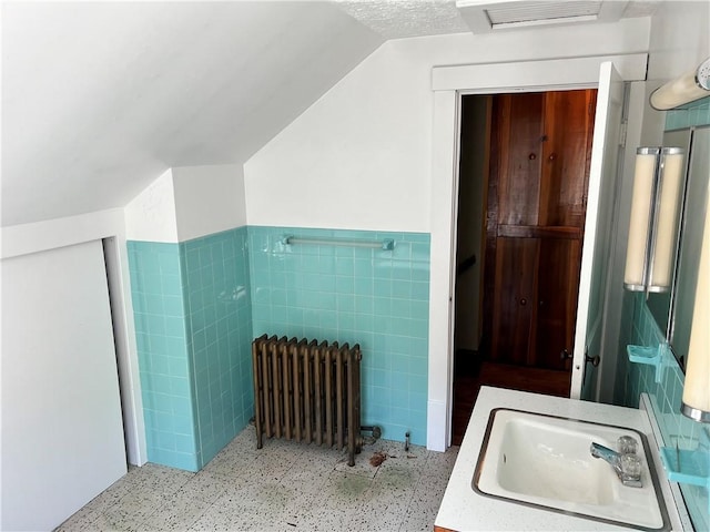 bathroom featuring visible vents, radiator heating unit, a sink, speckled floor, and tile walls