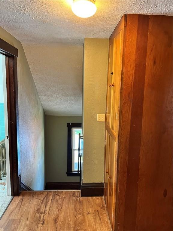 corridor featuring a textured ceiling, wood finished floors, and a textured wall