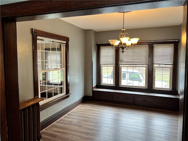 empty room with a notable chandelier, baseboards, wood finished floors, and a healthy amount of sunlight