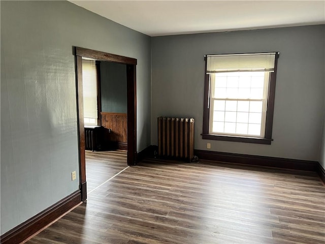 unfurnished room featuring radiator heating unit, baseboards, and wood finished floors