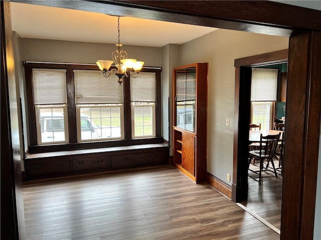 unfurnished dining area featuring a chandelier, a healthy amount of sunlight, baseboards, and wood finished floors