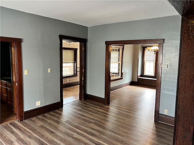 unfurnished room with a notable chandelier, dark wood finished floors, and baseboards