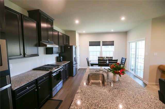 kitchen with appliances with stainless steel finishes, sink, light stone countertops, and dark hardwood / wood-style floors