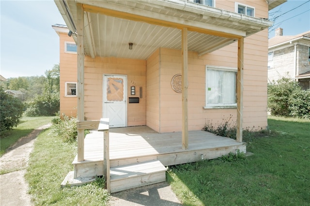 view of exterior entry with a lawn and a wooden deck