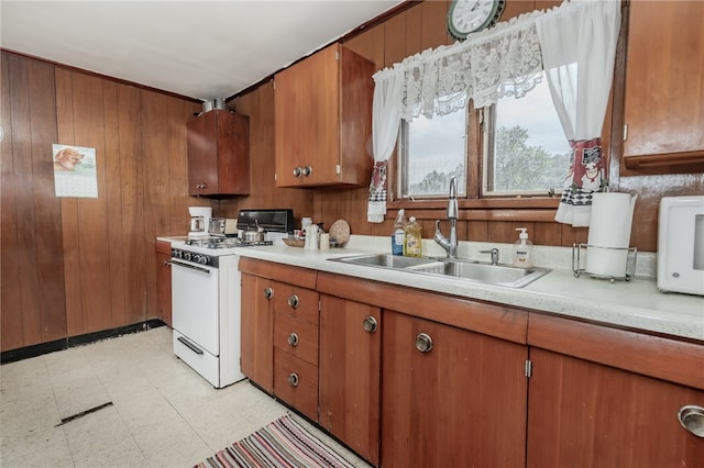 kitchen featuring white range with gas stovetop, wood walls, and sink