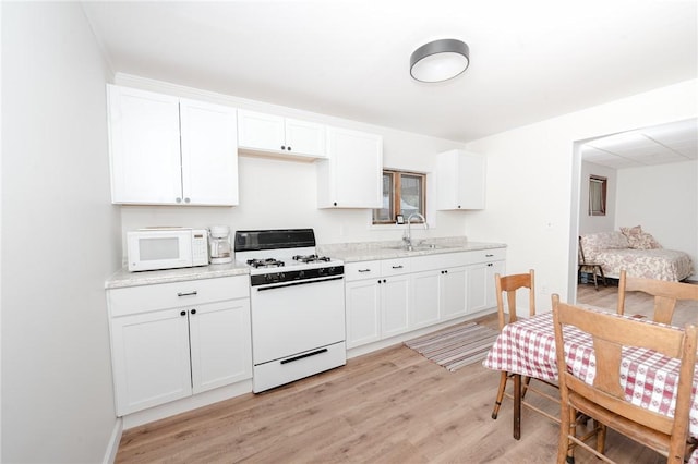 kitchen with white appliances, white cabinets, a sink, and light wood-style floors