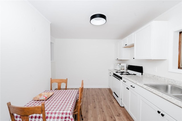 kitchen with white gas range oven, light countertops, light wood-style flooring, white cabinetry, and baseboards