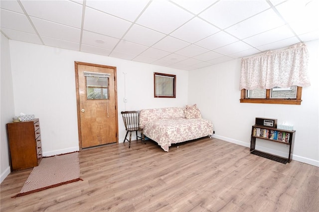 living area featuring baseboards, a drop ceiling, and light wood finished floors