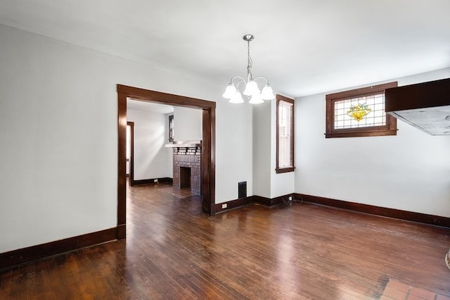 unfurnished room with a fireplace, dark wood-type flooring, and an inviting chandelier