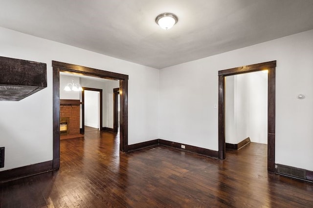 empty room featuring dark wood-type flooring, a chandelier, and a fireplace