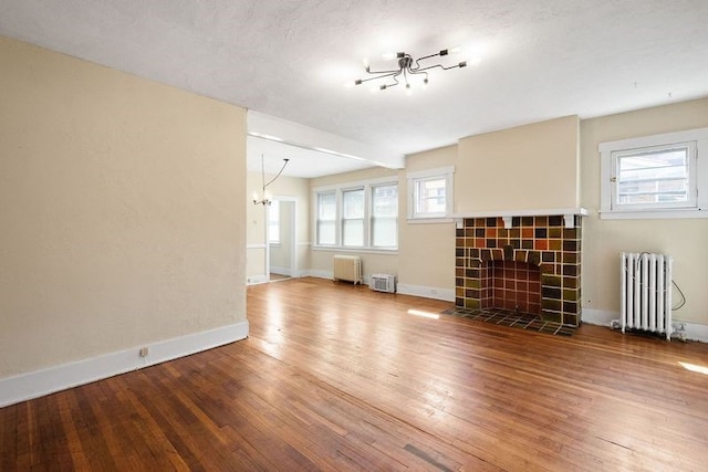 unfurnished living room featuring radiator heating unit, a healthy amount of sunlight, and a tiled fireplace