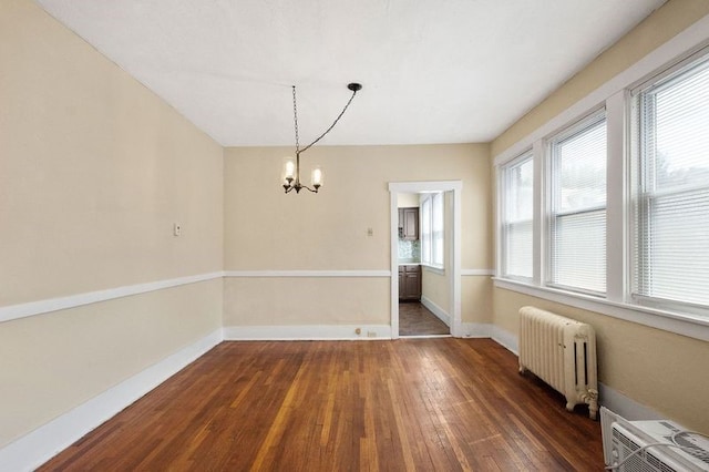 unfurnished dining area featuring dark wood-type flooring, radiator, and a notable chandelier