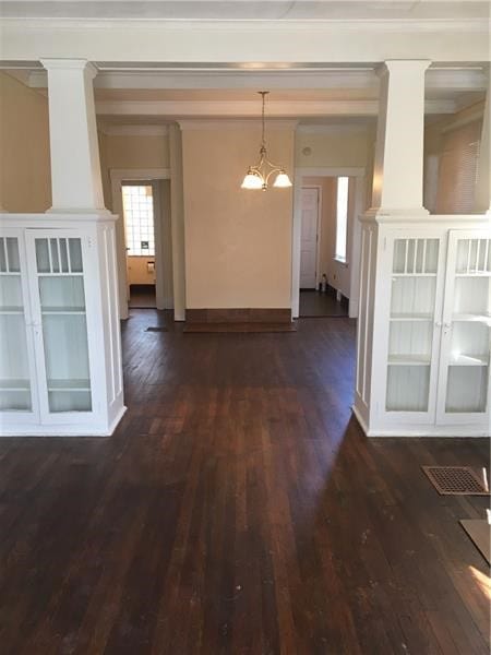 interior space featuring ornamental molding, dark wood-type flooring, a notable chandelier, and ornate columns