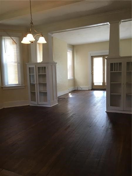 unfurnished living room featuring a healthy amount of sunlight, dark hardwood / wood-style floors, and a notable chandelier