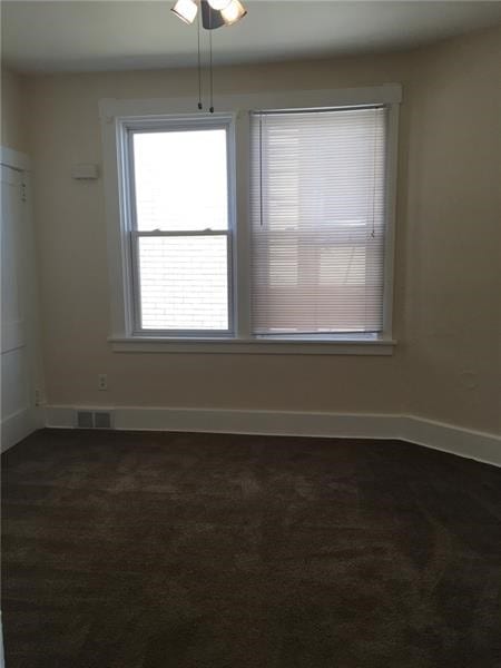 empty room with dark carpet, ceiling fan, and a healthy amount of sunlight