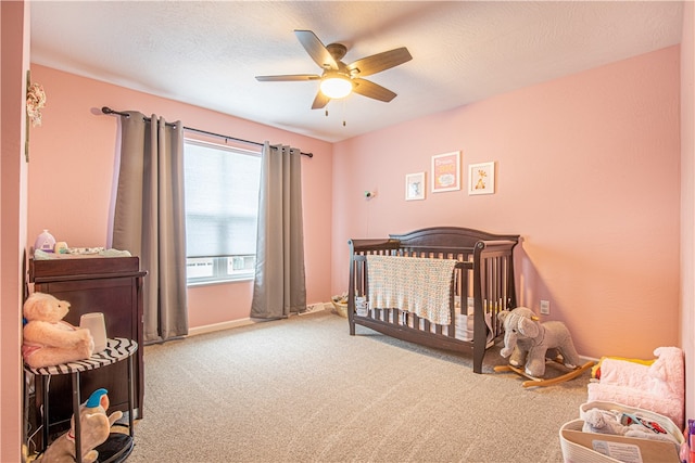 bedroom with ceiling fan, carpet, a textured ceiling, and a crib