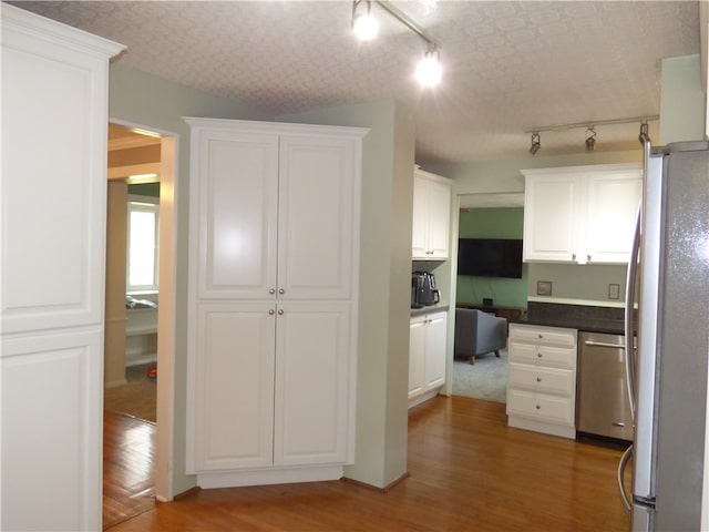 kitchen with built in desk, hardwood / wood-style flooring, appliances with stainless steel finishes, white cabinetry, and rail lighting