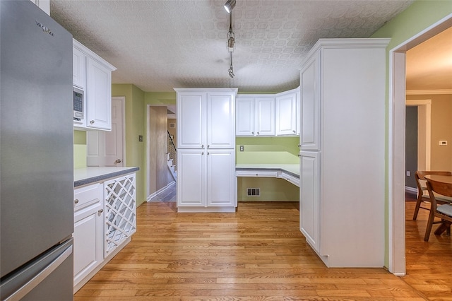 kitchen featuring a textured ceiling, light hardwood / wood-style flooring, appliances with stainless steel finishes, white cabinetry, and track lighting