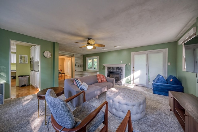 carpeted living room with a high end fireplace and ceiling fan