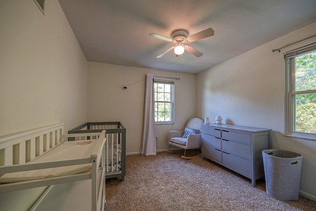 carpeted bedroom with ceiling fan and a nursery area