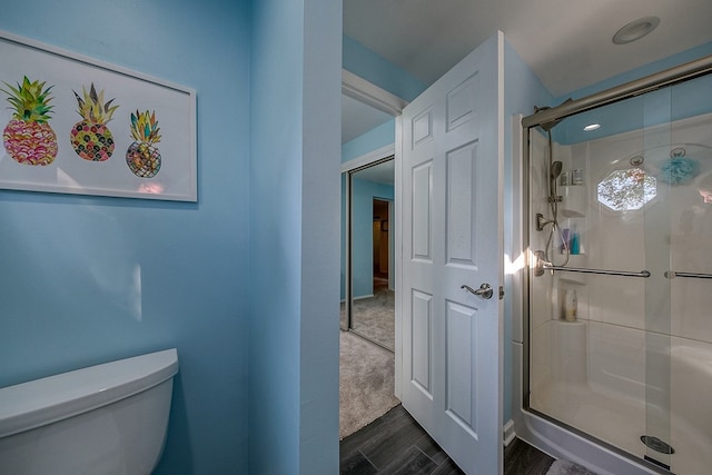 bathroom with toilet, an enclosed shower, and wood-type flooring