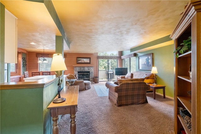 living room with carpet, a textured ceiling, wooden walls, and a stone fireplace