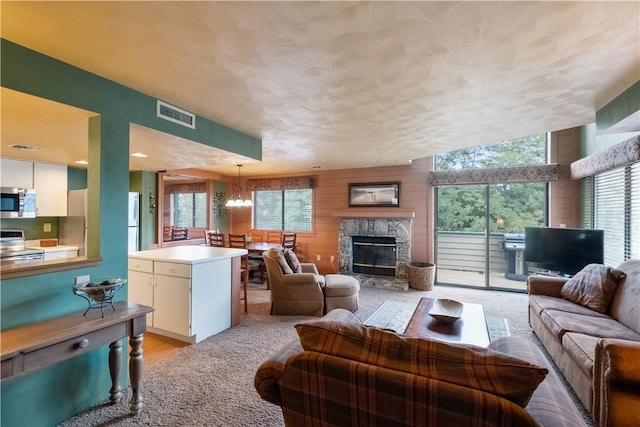 living room featuring a healthy amount of sunlight, wooden walls, a textured ceiling, and a stone fireplace