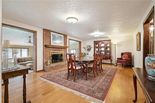 dining room featuring a textured ceiling, ceiling fan, light wood-type flooring, and a fireplace