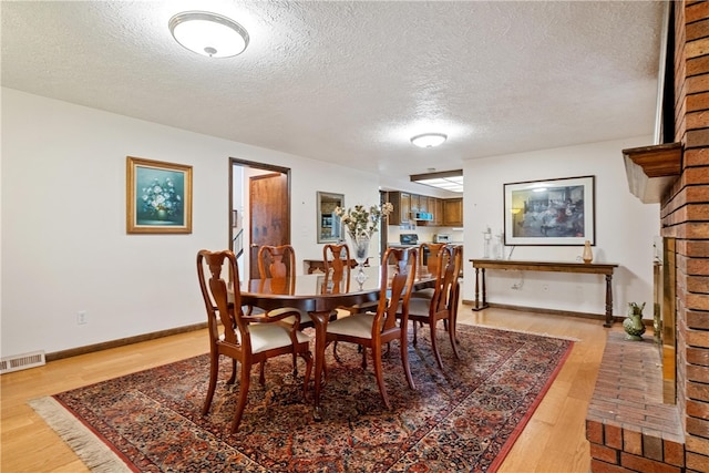 dining space featuring a brick fireplace, a textured ceiling, and light hardwood / wood-style flooring