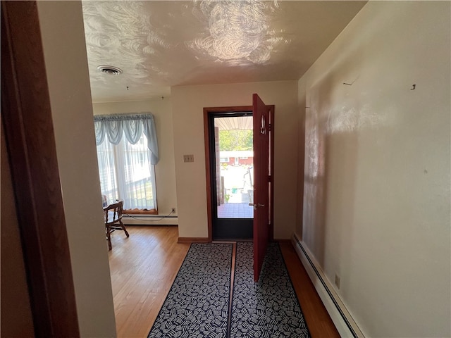 doorway to outside featuring light wood-type flooring, a baseboard heating unit, and a textured ceiling