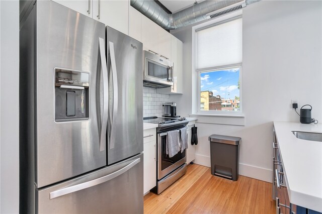 kitchen featuring light hardwood / wood-style flooring, stainless steel appliances, backsplash, and white cabinetry