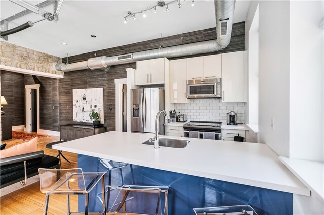 kitchen with sink, light hardwood / wood-style flooring, white cabinetry, appliances with stainless steel finishes, and a breakfast bar