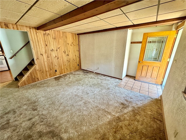 unfurnished room featuring beamed ceiling, carpet floors, and wood walls