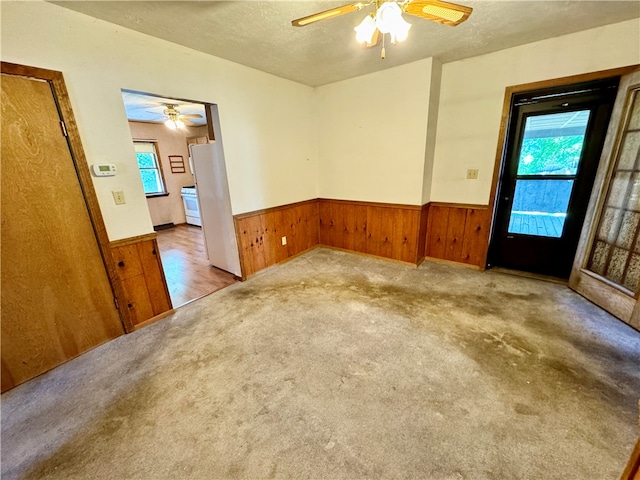 carpeted empty room with wooden walls, ceiling fan, and a textured ceiling