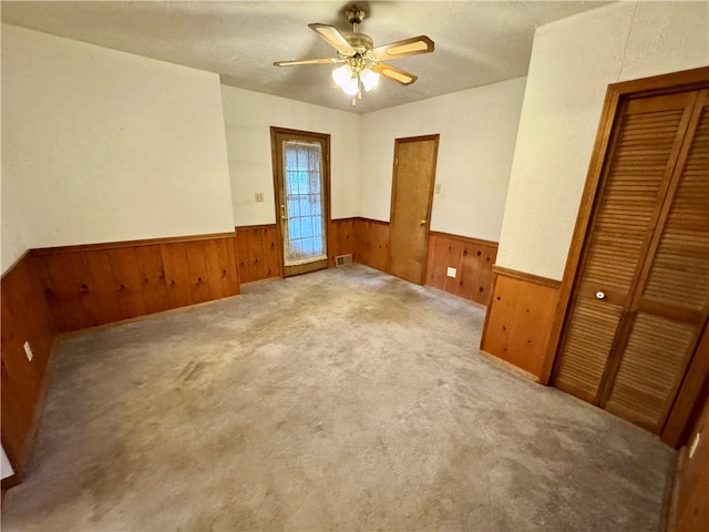 carpeted spare room with ceiling fan, wood walls, and a textured ceiling