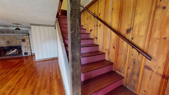 stairs featuring a textured ceiling, wood-type flooring, wooden walls, and a stone fireplace