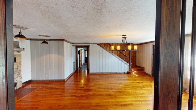 empty room with wood walls, hardwood / wood-style flooring, a chandelier, and crown molding