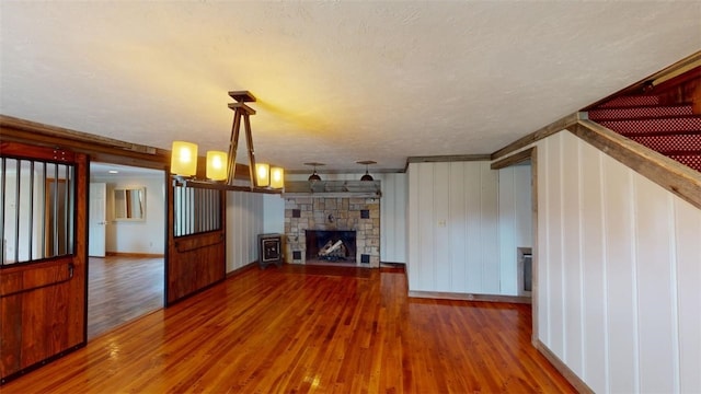 unfurnished living room with a textured ceiling, wood walls, a fireplace, a chandelier, and hardwood / wood-style flooring