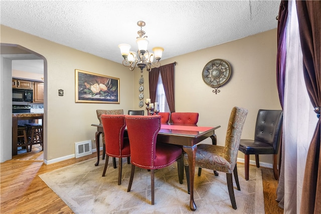 dining room with light wood-type flooring, a textured ceiling, and a notable chandelier