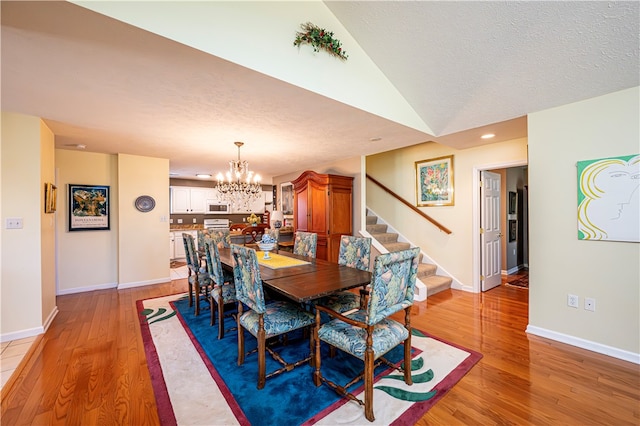 dining area featuring vaulted ceiling, a textured ceiling, hardwood / wood-style floors, and a notable chandelier