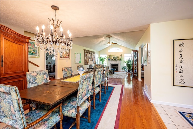 dining space featuring ceiling fan with notable chandelier, vaulted ceiling, a textured ceiling, and light hardwood / wood-style floors