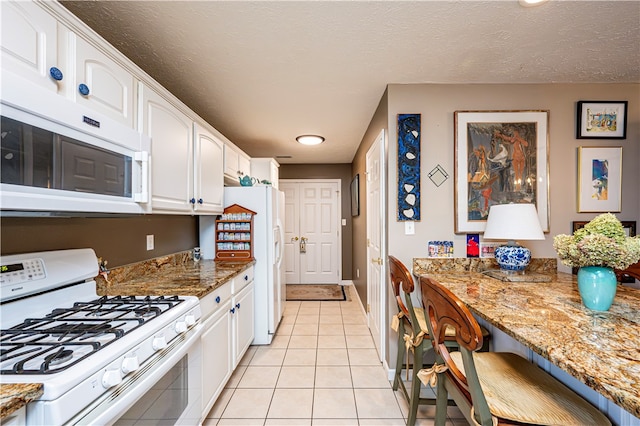 kitchen with white appliances, white cabinetry, stone countertops, and light tile patterned flooring