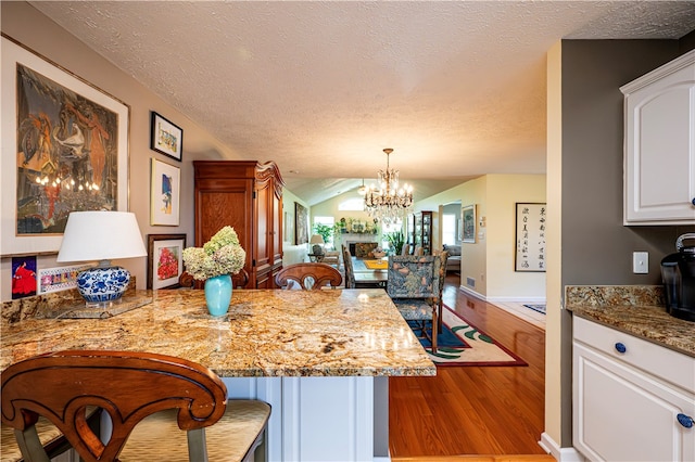 kitchen with white cabinets, light wood-type flooring, light stone counters, a chandelier, and lofted ceiling