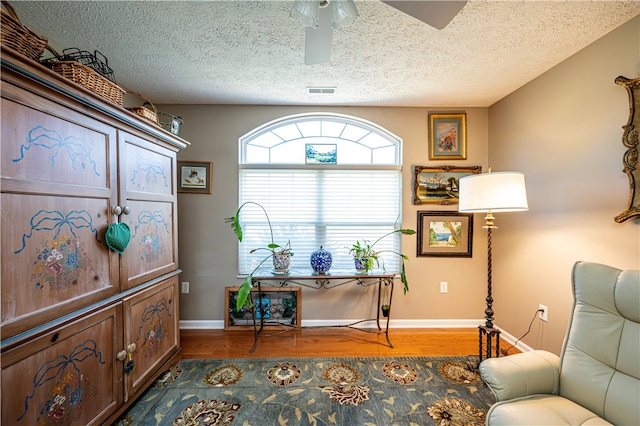 living area with a textured ceiling, hardwood / wood-style floors, and ceiling fan