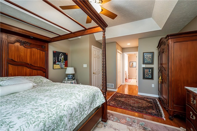 bedroom with ceiling fan, hardwood / wood-style flooring, ensuite bathroom, and a textured ceiling