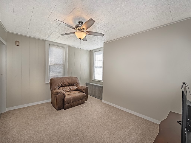 living area featuring light colored carpet, ceiling fan, wood walls, and radiator heating unit