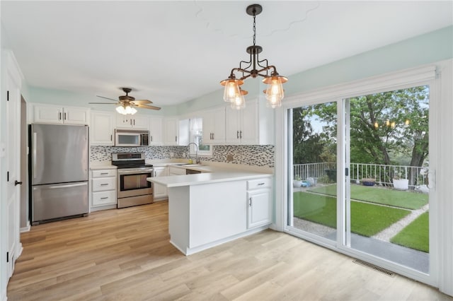 kitchen featuring ceiling fan with notable chandelier, white cabinetry, decorative light fixtures, kitchen peninsula, and appliances with stainless steel finishes